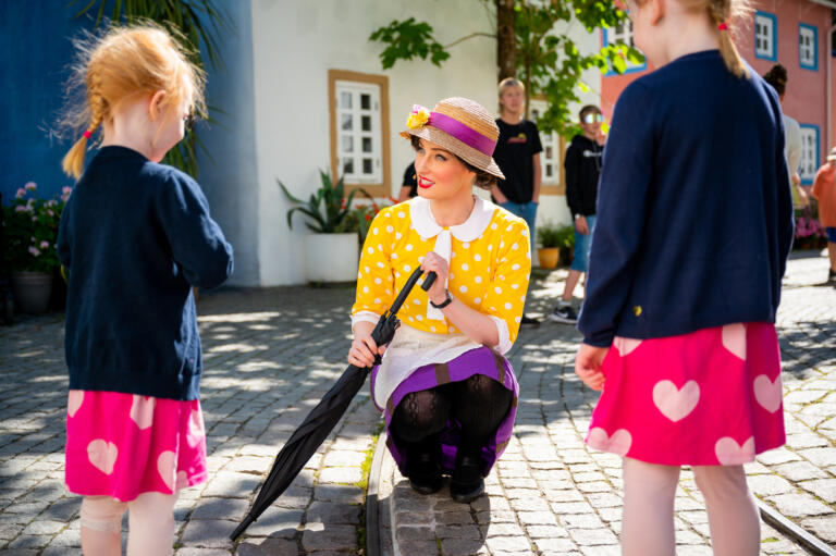 Nysgjerrige og oppmerksomme, følger to små jenter med når tante Sofie sitter ned på huk for å snakke med dem i Kardemomme by.